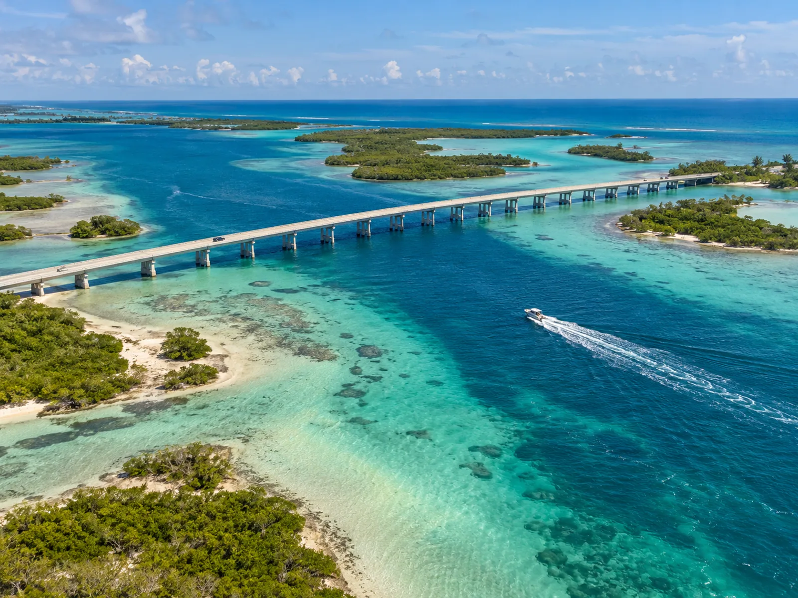 Aerial view of a coastal bridge and a boat crossing clear turquoise water